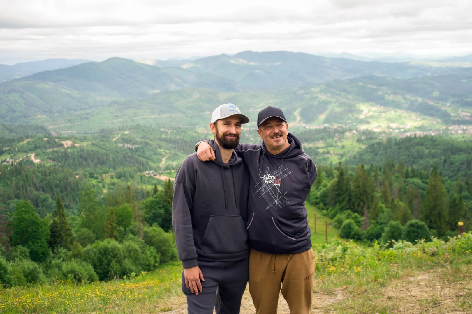 Two people standing together against a mountain landscape