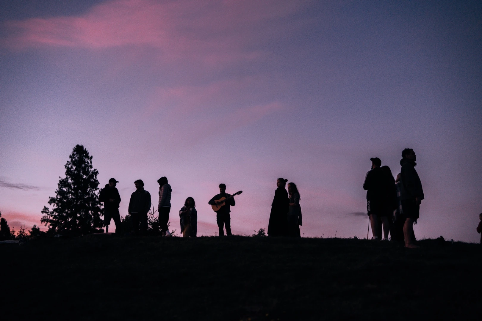 A group with a guitar silhouetted against the evening sky